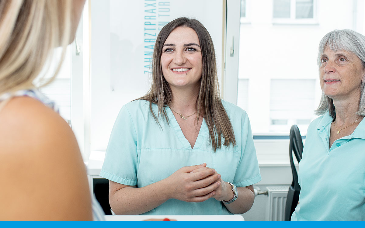 Lächelende ZFA am Empfang im Gespräch mit einer Patientin in Darmstadt.